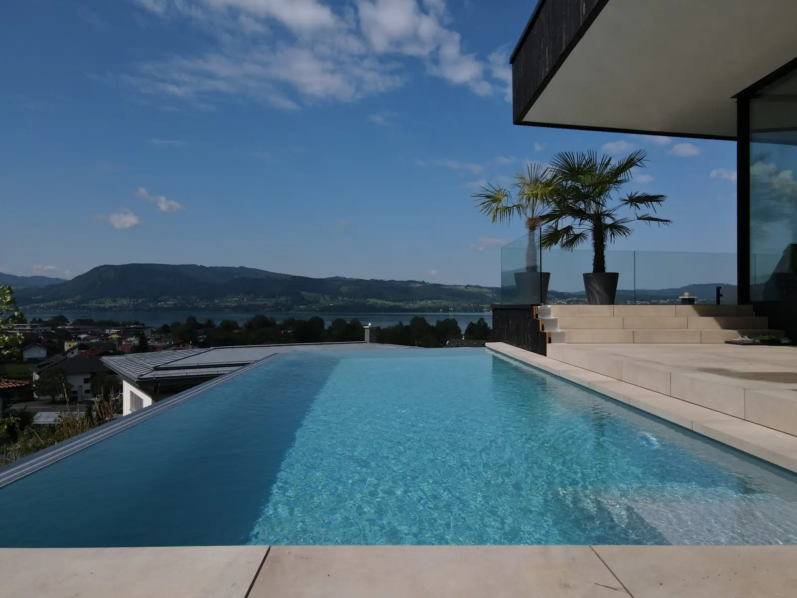 Edelstahlpool mit Überlaufkante auf einer Terrasse, dahinter der Attersee