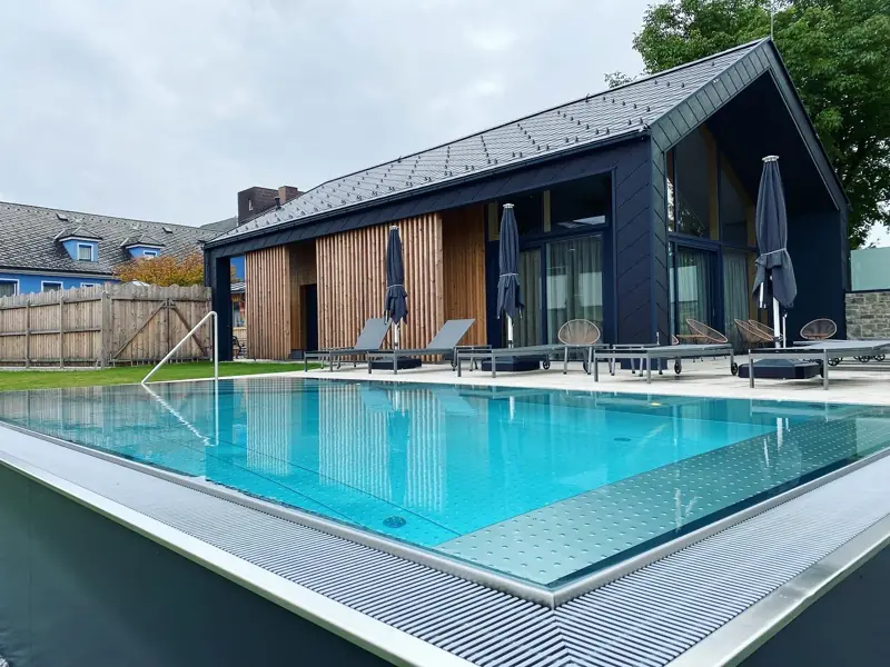 Edelstahlpool mit Überlaufrinne vor einem Holzhaus mit Satteldach