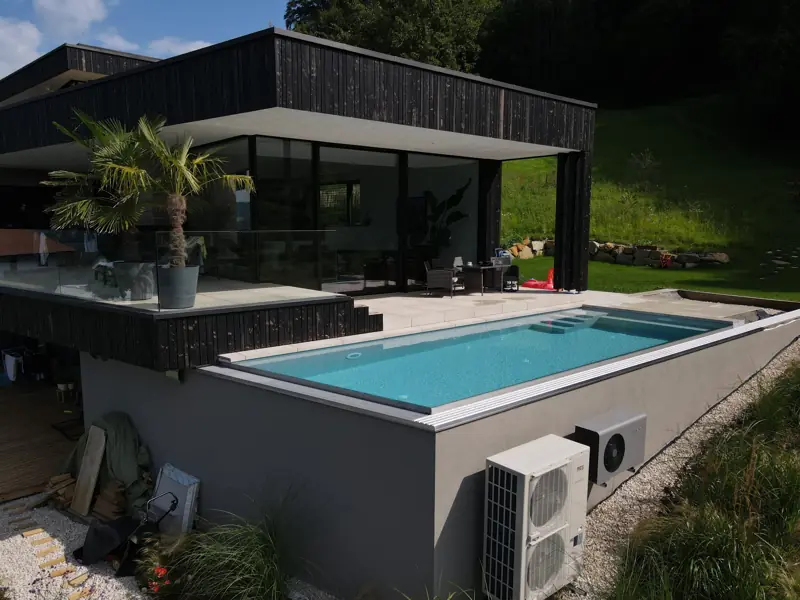 Erhöht gebauter Pool vor einem modernen Haus mit dunkler Fassade