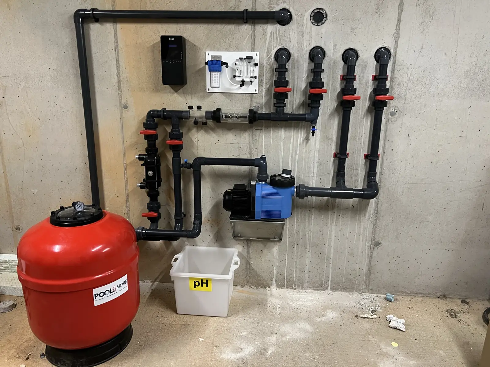 Technikraum mit rotem Sandfilter, blauer Pumpe, Steuerung, Messzelle, pH-Behälter und Rohrleitungen an einer Betonwand
